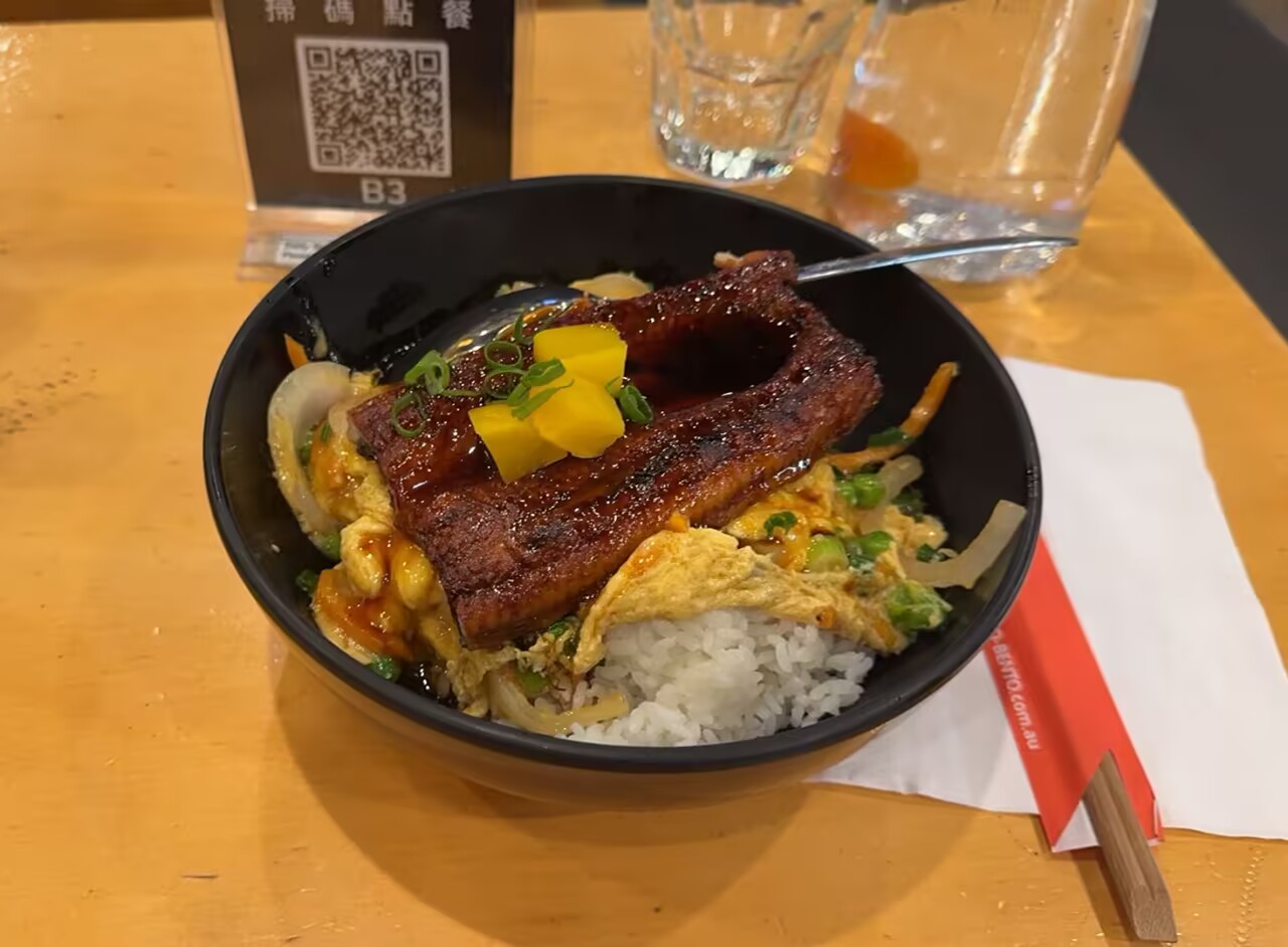 我的午饭:一碗铺着烤鳗鱼、鸡蛋和黄色腌菜的米饭。